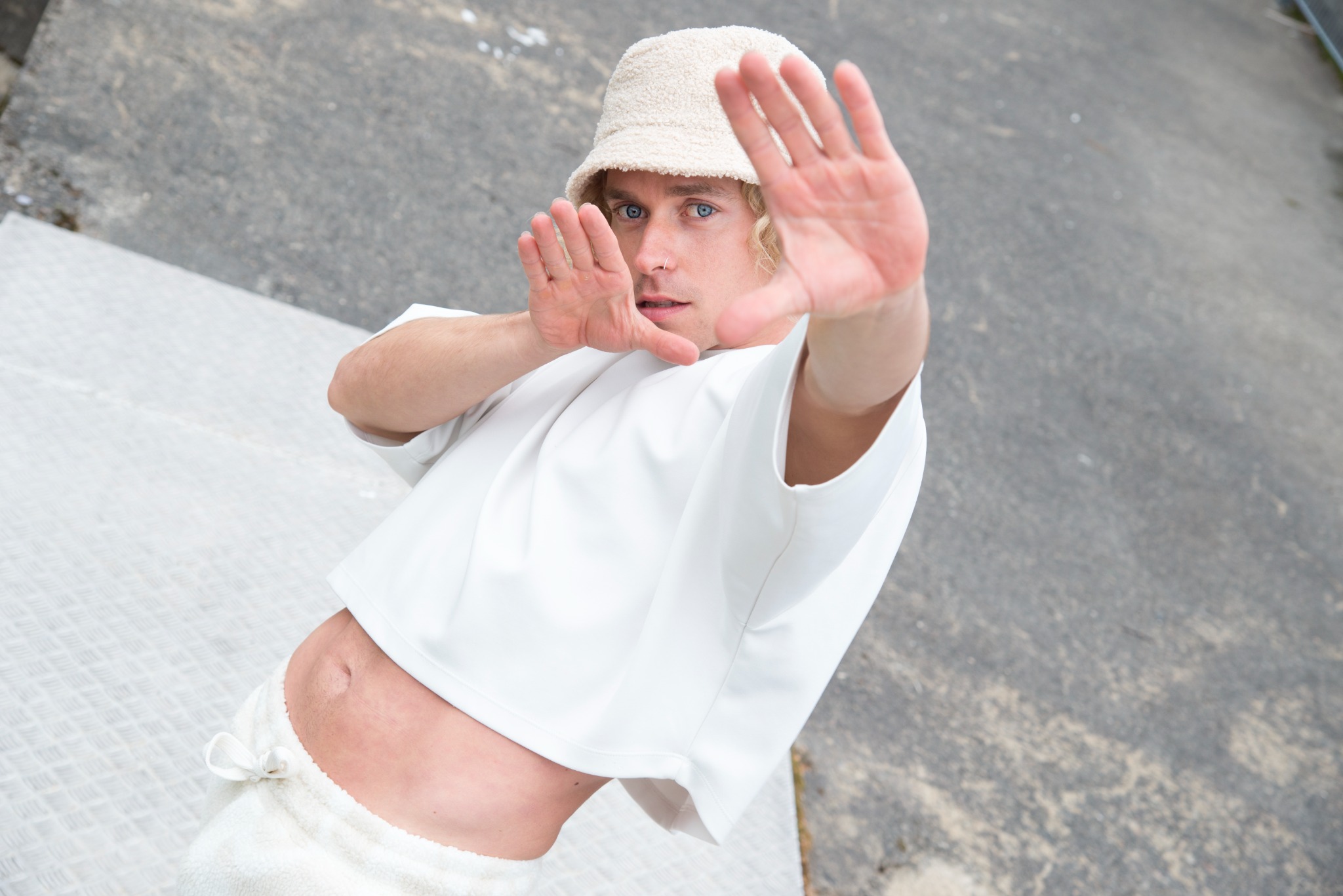 Toni in a white outfit and bucket hat, framing the camera with his hands